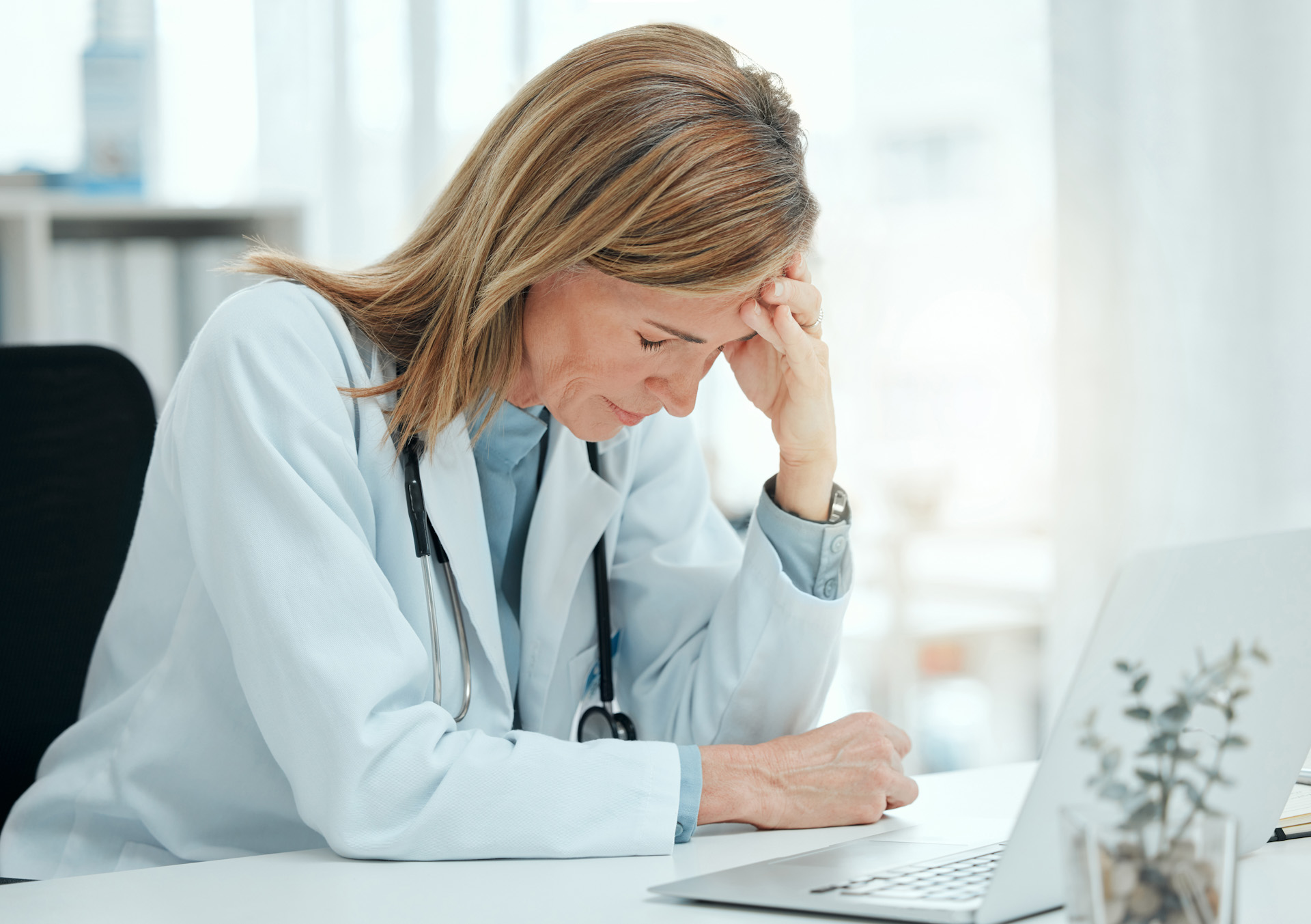 Physician frustrated at a laptop managing complex billing paperwork